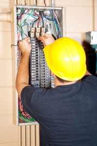 man with yellow hard hat installing panel for breakers